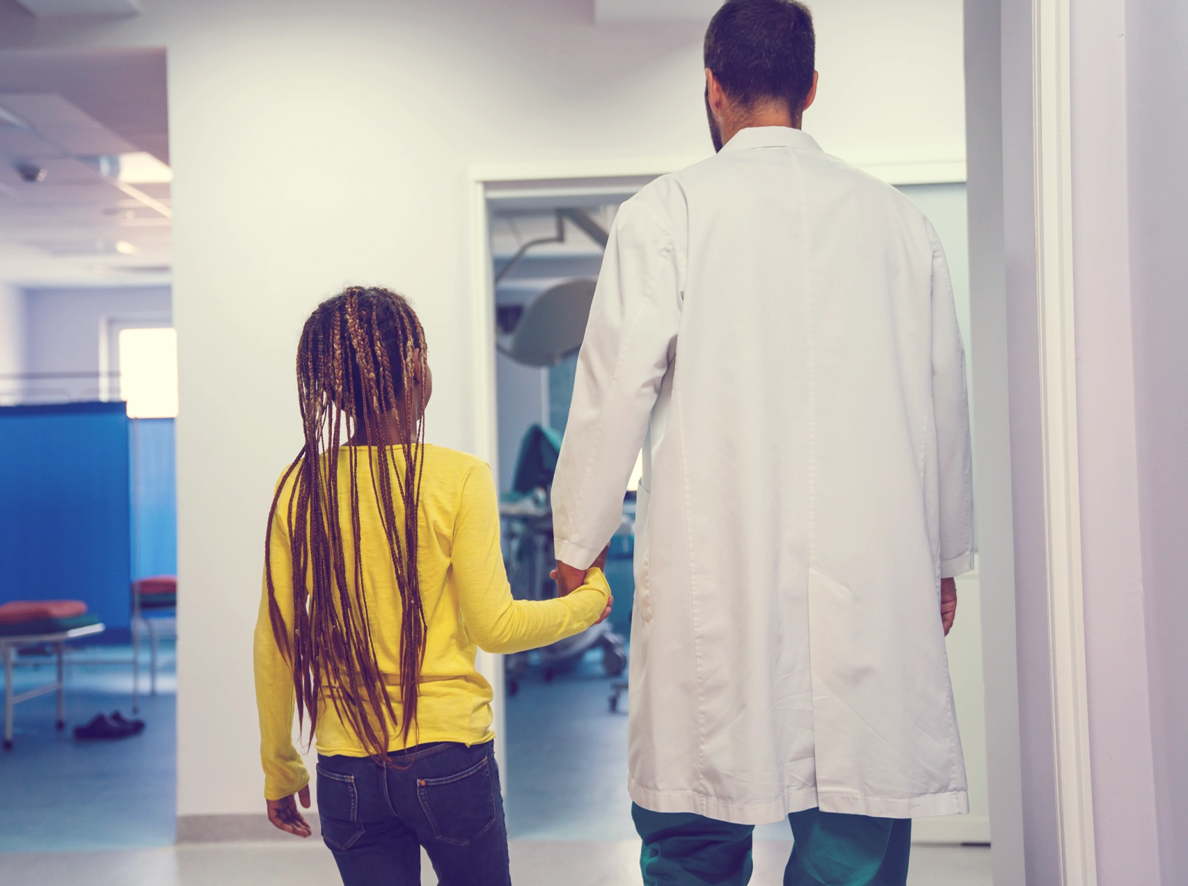 Young girl and doctor walk toward exam room in a hospital setting