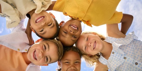 Diverse group of children smiling. They are Linking Arms Looking Down Into Camera.