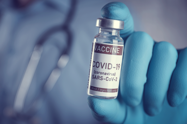 A close up image of a doctor holding a vial with a COVID-19 label.