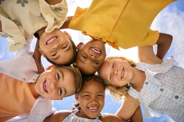 Diverse group of children smiling. They are Linking Arms Looking Down Into Camera.