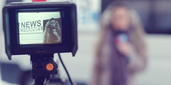 Image focused on the screen of a camera which is recording a journalist