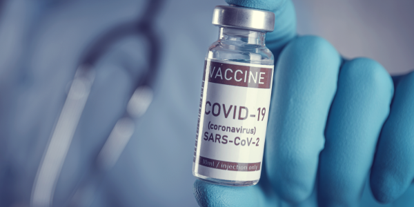 A close up image of a doctor holding a vial with a COVID-19 label.